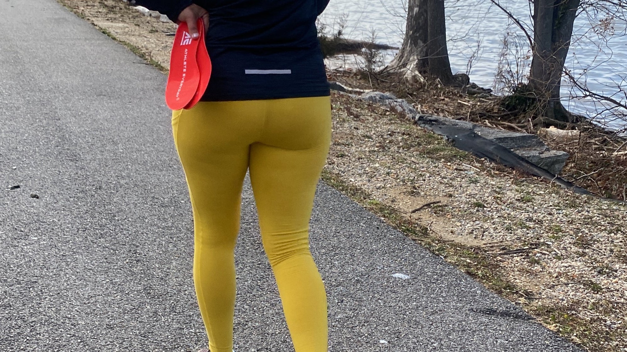 Person running on a road with bare trees and a sidewalk in the background